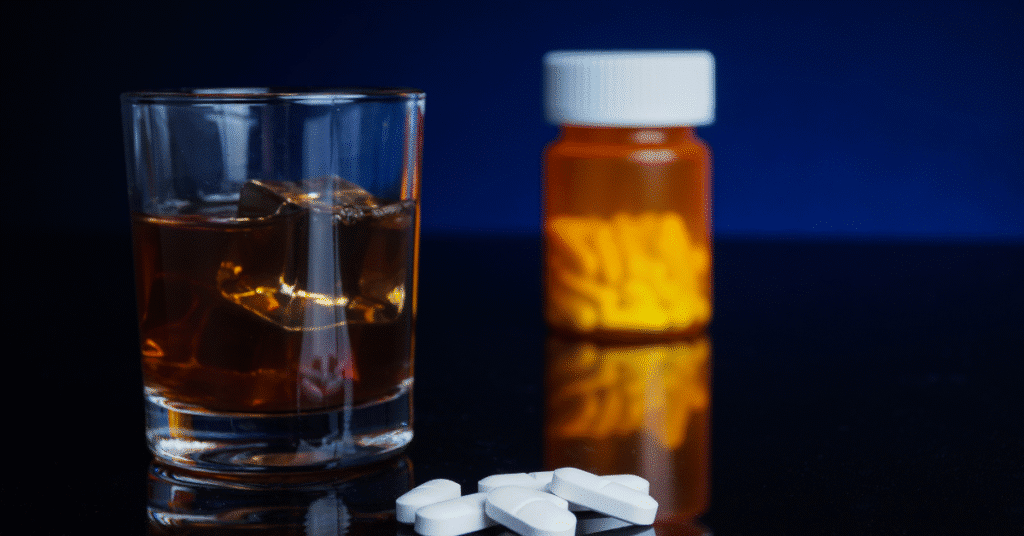 Glass of liquor with ice beside a prescription pill bottle