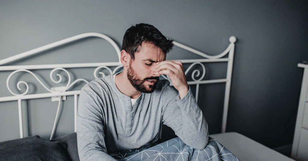 Man in bed holding head, showing signs of hangxiety.