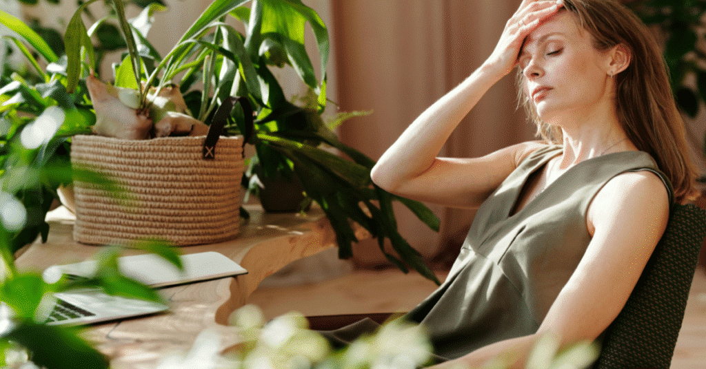 Stressed woman sitting indoors with hand on forehead