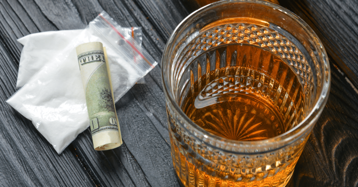 Mixing alcohol and cocaine – glass of liquor with cocaine powder