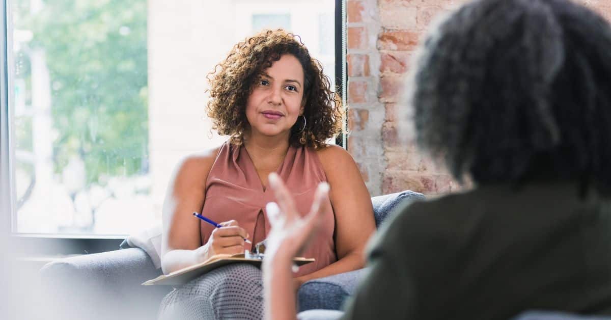 A therapist listens and takes notes during a women’s mental health counseling session