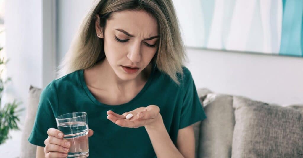 Woman holding a pill and a glass of water