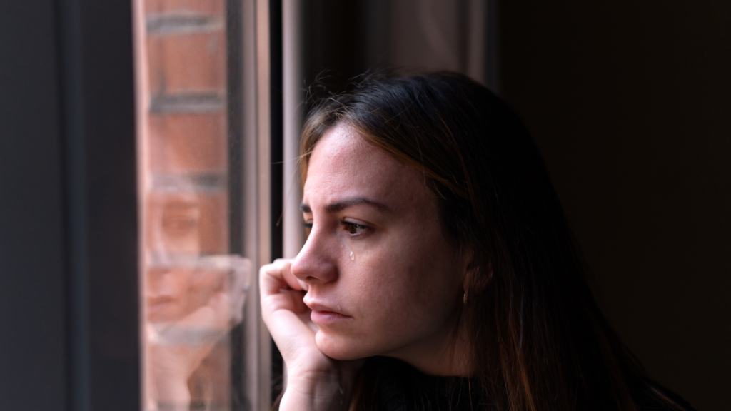 Young woman looking out a window feeling anxious