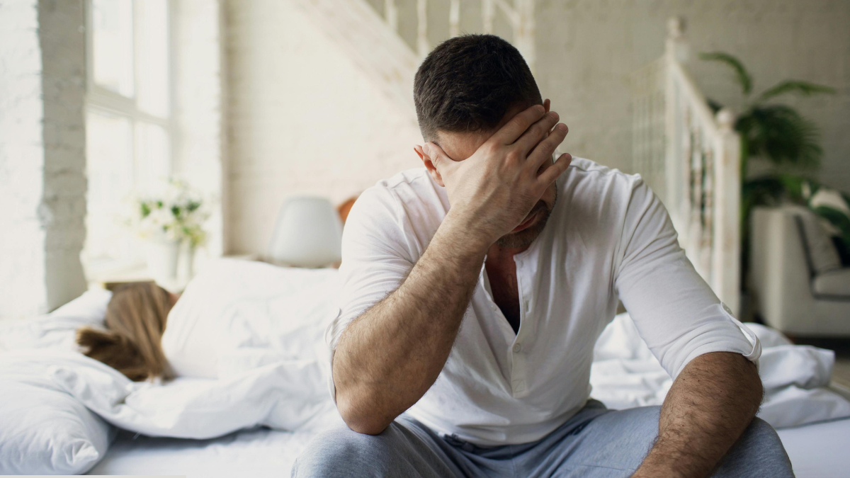 Homepage 5 Man sitting on the edge of a bed holding his head in frustration