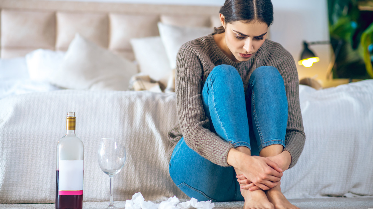 Homepage 5 Woman sitting on the floor hugging her knees beside a bottle of wine and an empty glass
