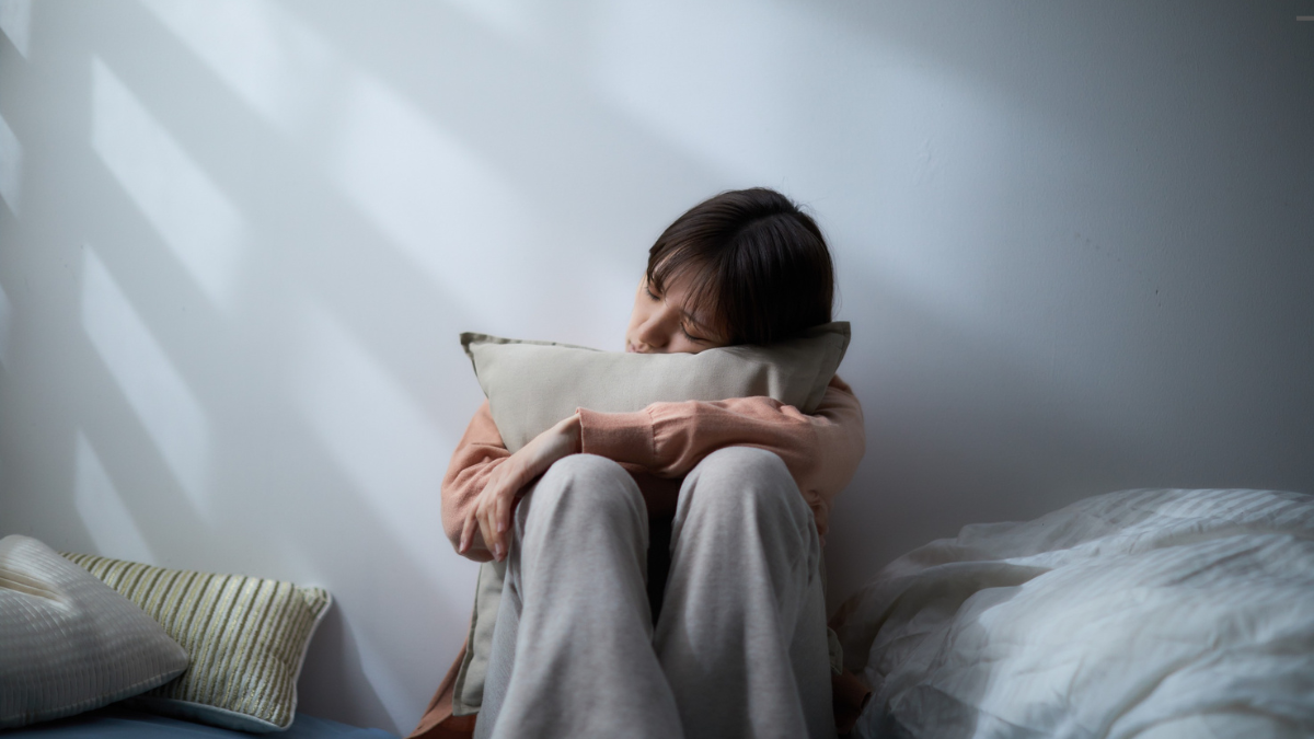 Woman hugging a pillow against a wall, looking emotionally withdrawn