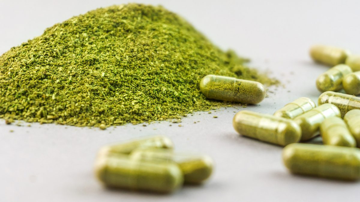 Pile of green kratom powder next to kratom capsules